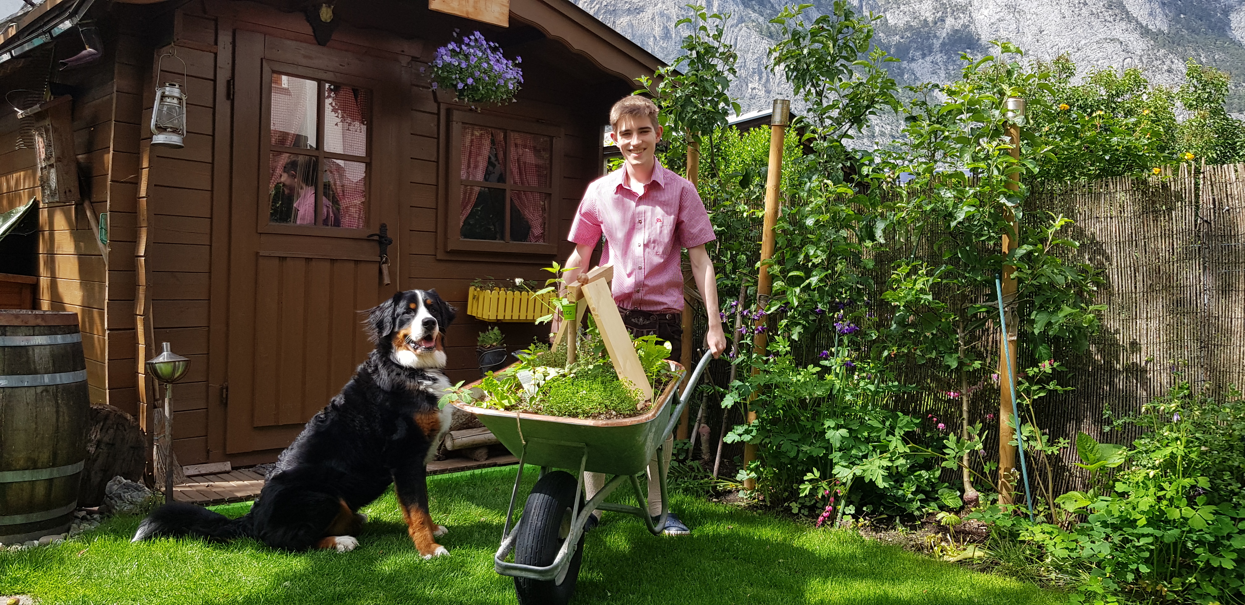 Philip Kuster mit einer Schubkarre und seinem Hund vor einem Gartenhäuschen