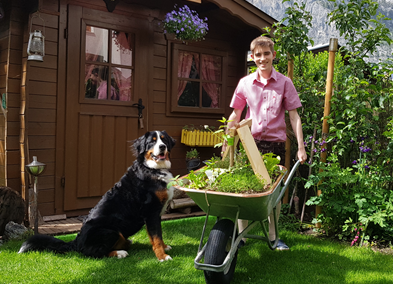 Philip Kuster mit einem Schubkarren und seinem Hund vor einem Gartenhäuschen